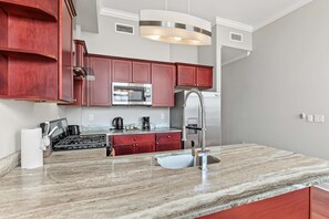 A modern kitchen with a marble countertop, stainless steel appliances, and red cabinetry. - Polished Metro 1BD Retreat | Top Eats | Sleeps 2 (Philadelphia)