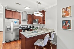 A modern kitchen with a central island, stainless steel appliances, and wooden cabinetry. - Stylish City Escape | Comfy Studio Onsite Fitness (Philadelphia)