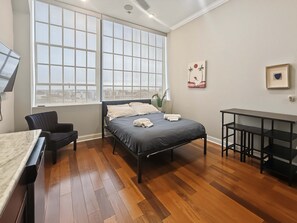 A modern bedroom with a bed, a desk, a chair, and a large window. - Prime Studio City Hideaway | Gym Pass | Fits 2 (Philadelphia)