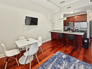 A compact kitchen with a dining area, a flat-screen TV mounted on the wall, and a stainless steel refrigerator. - Posh Urban 1BR | Gourmet District | Welcomes 2 (Philadelphia)