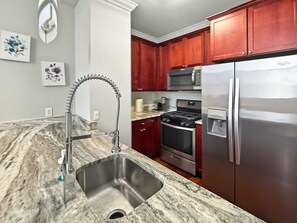 A modern kitchen with a stainless steel sink, a gas stove, a microwave, and a refrigerator. - Posh Urban 1BR | Gourmet District | Welcomes 2 (Philadelphia)