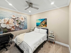 Ein Schlafzimmer mit einem Bett, einem Schreibtisch, einem Stuhl, einem Deckenventilator und zwei Wandleuchten.