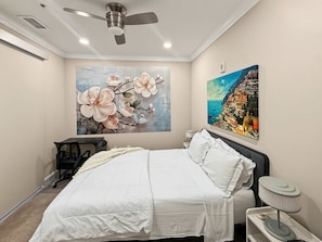 A bedroom with a bed, a desk, a chair, a ceiling fan, and two paintings on the wall. - Chic 1BR City Haven | Near Dining | Perfect for 2 (Philadelphia)