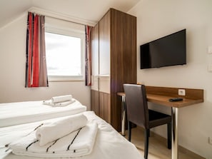 Une chambre d’hôtel avec un lit, un bureau, une chaise, une télévision et une fenêtre avec des rideaux.