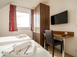 Una habitación de hotel con cama, escritorio, silla, televisor y ventana con cortinas.