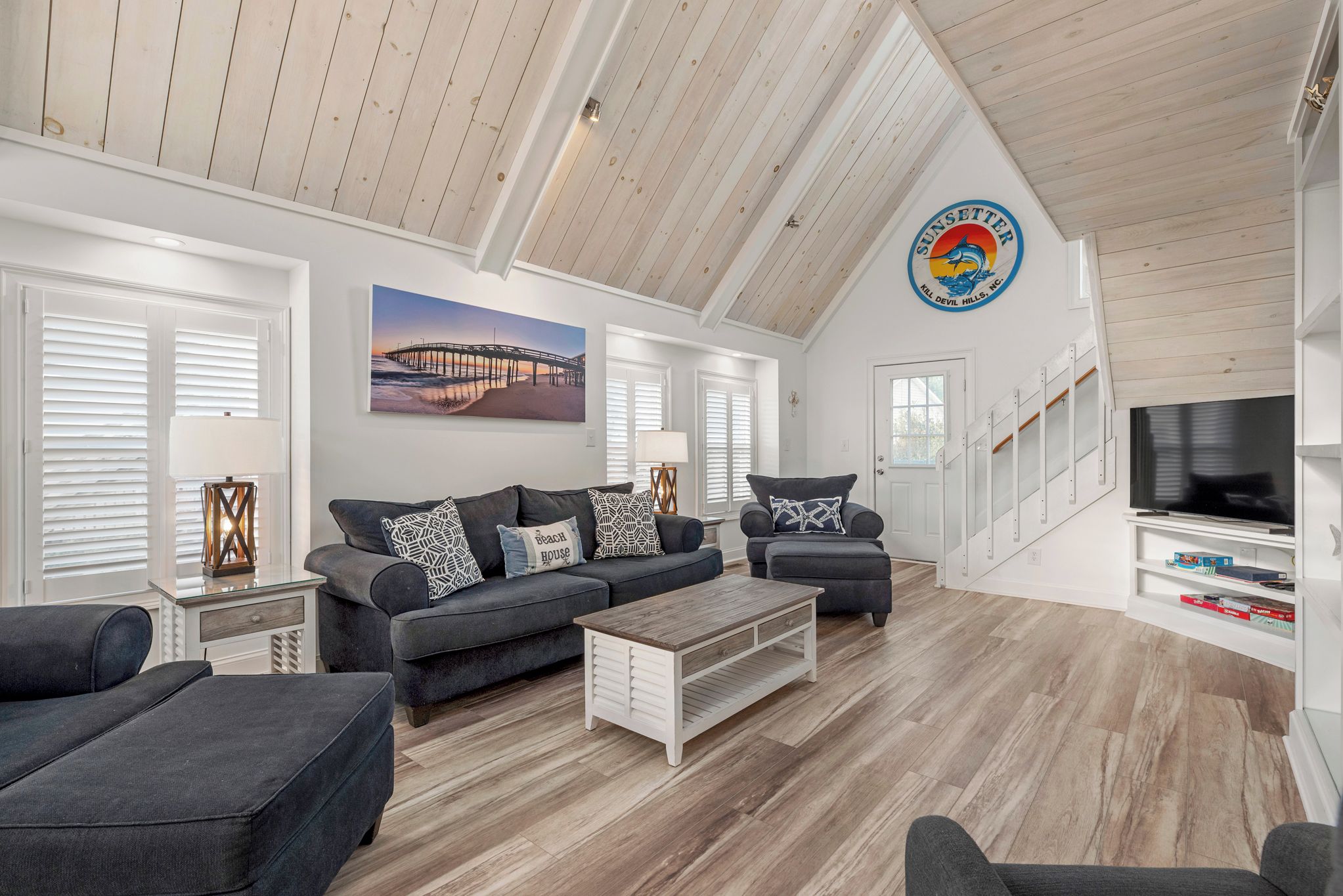 A spacious living room with a high ceiling, a large TV, and a painting of a pier.