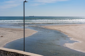 A beach with a clear view of the ocean, a street lamp, and a distant ship. - Spacious Beachfront Retreat | Stunning Ocean Views (Cape Town)