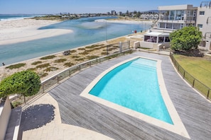 A swimming pool with a wooden deck, a beach, and a cityscape in the background. - Spacious Beachfront Retreat | Stunning Ocean Views (Cape Town)