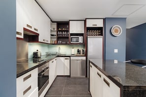 A compact kitchen with white cabinets, a microwave, a dishwasher, and a coffee maker. - Retro CBD Escape | Pool and City Living (Cape Town)