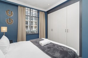 A hotel room with a bed, a large wardrobe, a window with curtains, and two wall-mounted decorative items. - Retro CBD Escape | Pool and City Living (Cape Town)