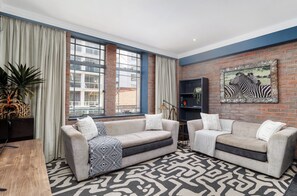 A modern living room with two sofas, a patterned rug, a bookshelf, and a large window with curtains. - Retro CBD Escape | Pool and City Living (Cape Town)