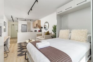 A modern hotel room with a large bed, a desk, a chair, a sofa, and a kitchenette. - The Sage | Central Sea Point Stay (Cape Town)