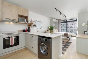 A modern kitchen with a built-in washing machine, a microwave, and a dining area with a view. - The Sage | Central Sea Point Stay (Cape Town)