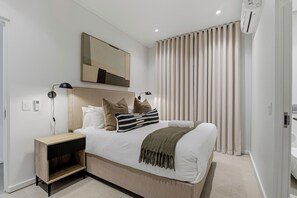 A modern bedroom with a bed, bedside tables, a mirror, and a window with curtains. - Luxe Modern Apartment | Ocean Views | Aircon (Umhlanga)