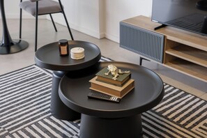A modern living room with two black round tables, a small decorative sculpture, a remote control, and a candle on one table. - Luxe Modern Apartment | Ocean Views | Aircon (Umhlanga)