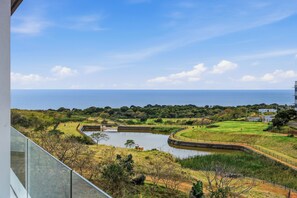A coastal landscape with a body of water, grassy areas, and a distant view of the sea. - Luxe Modern Apartment | Ocean Views | Aircon (Umhlanga)