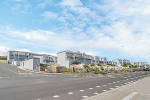 A modern residential area with multi-story buildings, a clear road, and a pedestrian pathway. - Stylish 2 Bed Apartment | Big Bay Beach Club (Cape Town)