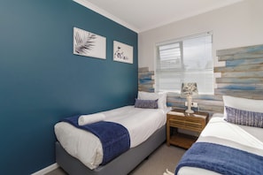 A bedroom with two beds, a nightstand, a lamp, and artwork on the wall. - Stylish 2 Bed Apartment | Big Bay Beach Club (Cape Town)