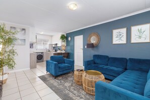 Una sala de estar moderna con sofás azules, una cocina al fondo y un comedor.