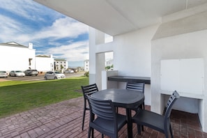 Un patio al aire libre con una mesa y sillas, un muro blanco y vista a una calle con coches estacionados.