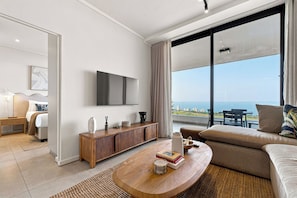 Ein modernes Wohnzimmer mit einem großen Fenster, einem Flachbildfernseher, einem Holztisch und einem Sofa.