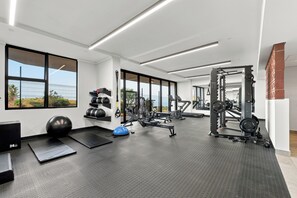 Ein Fitnessstudio mit unterschiedlichen Trainingsgeräten, großen Fenstern und einem Boden aus Gummimatten.