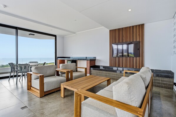 A modern living area with a sofa, chairs, a coffee table, and a TV mounted on a wooden panel wall. - Stylish Umhlanga 2Bed | Aircon and Gym (Umhlanga)