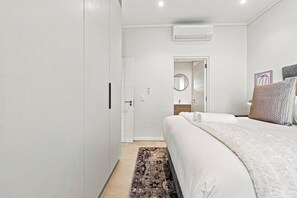 A bedroom with a bed, a bedside table, a mirror, and a wall-mounted air conditioner. - Stylish Umhlanga 2Bed | Aircon and Gym (Umhlanga)