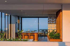 A modern outdoor dining area with a brick column, metal chairs, and a glass partition. - Stylish Umhlanga 2Bed | Aircon and Gym (Umhlanga)