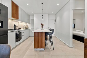 Eine moderne Küche mit Kochinsel, ein Essbereich mit Barhocker und ein separates Schlafzimmer mit Bett und Fenster.