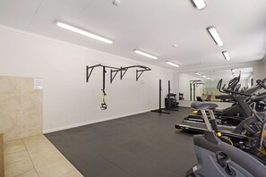 Een fitnessruimte met trainingsapparatuur, waaronder een loopband, hometrainers en een optrekstang.