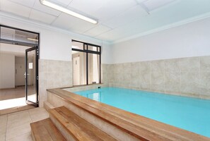 An indoor swimming pool with clear blue water, tiled walls, and a wooden bench. - Elegant De Waterkant Stay | Pool and Gym (Cape Town)