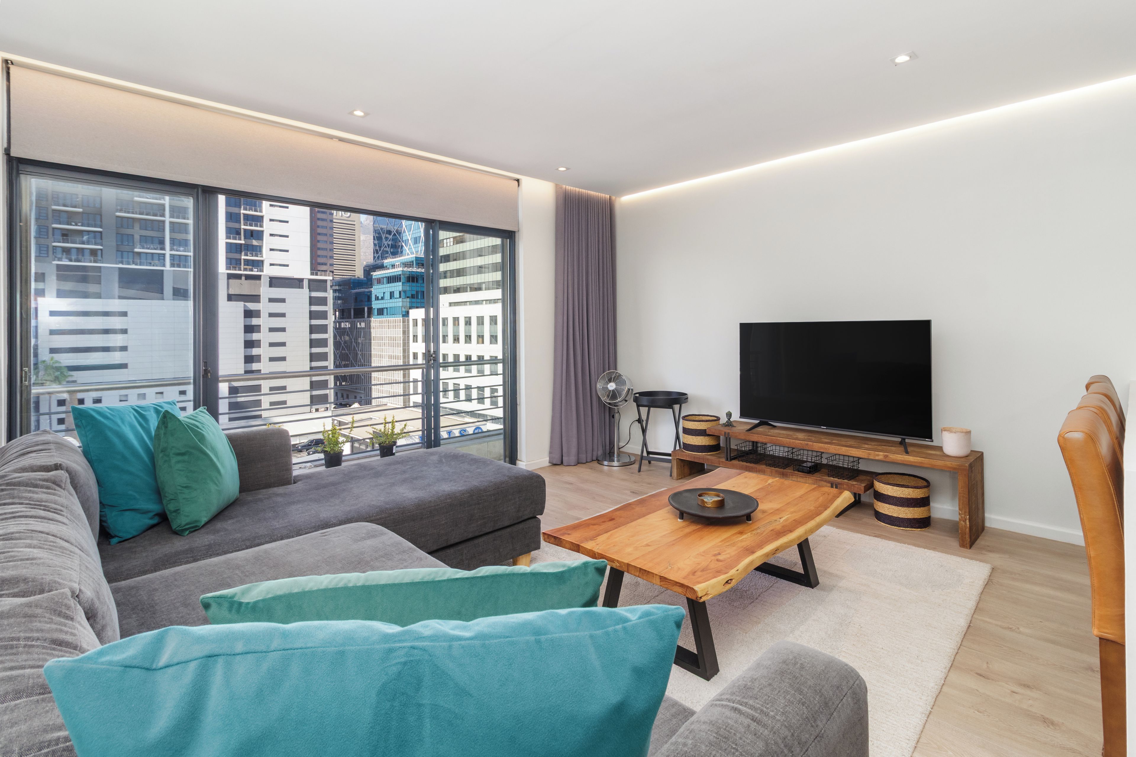 A modern living room with a sofa, a coffee table, a TV, and a view of the city through large windows.