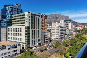A cityscape with modern buildings, a prominent office tower, and a mountain in the background. - Elegant De Waterkant Stay | Pool and Gym (Cape Town)