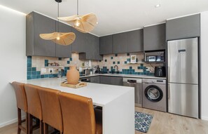 Een moderne keuken met grijze kastjes, een roestvrijstalen koelkast, een ingebouwde magnetron en een wasmachine.