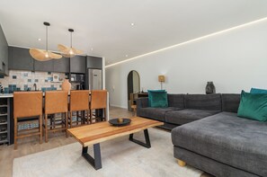 A modern living room with a grey sofa, wooden dining table, and chairs. - Elegant De Waterkant Stay | Pool and Gym (Cape Town)