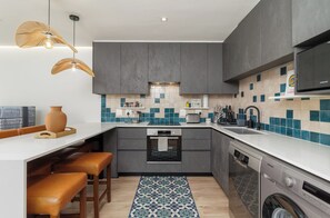 Une cuisine moderne avec des meubles gris, un plan de travail blanc, un lave-vaisselle encastré et un lave-linge.
