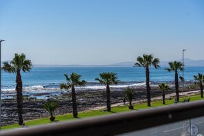 A coastal view with palm trees and a rocky beach. - Stylish Seaside Stay | Ocean Views and Balcony (Cape Town)