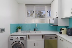 A compact kitchen with a washing machine, dishwasher, and a microwave. - Stylish Seaside Stay | Ocean Views and Balcony (Cape Town)