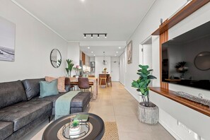 A modern living room with a sofa, coffee table, and a dining area with chairs and a table. - Umhlanga 2BR | Aircon, Balcony and Gym (Umhlanga)