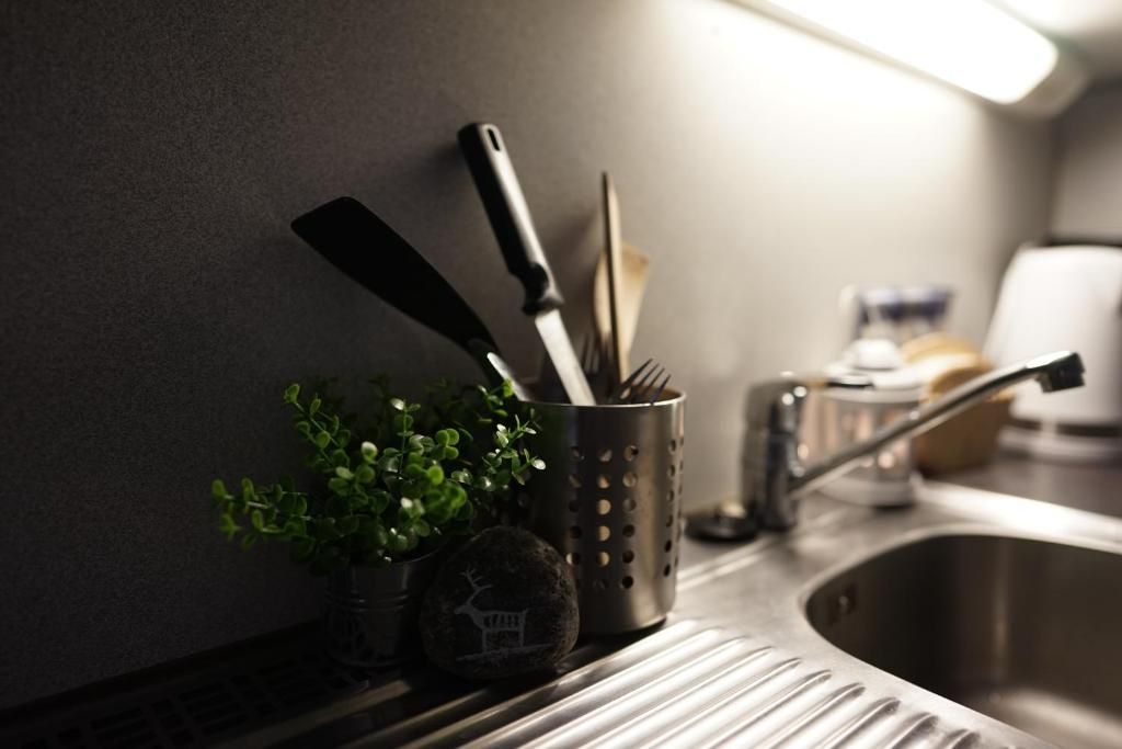 Una encimera de cocina con un lavamanos de acero inoxidable, una planta en maceta y utensilios de cocina.