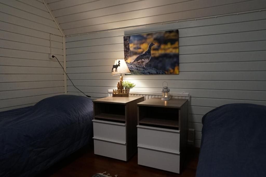 Ein Zimmer mit zwei Betten, einem Nachttisch mit Lampe, einem Bild an der Wand und einer kleinen Pflanze.