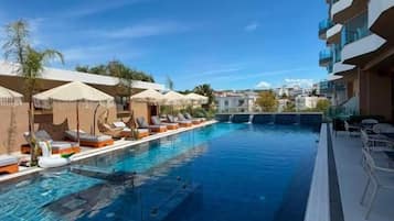 Una piscina con sillas de descanso y sombrillas, rodeada por un edificio con balcones.