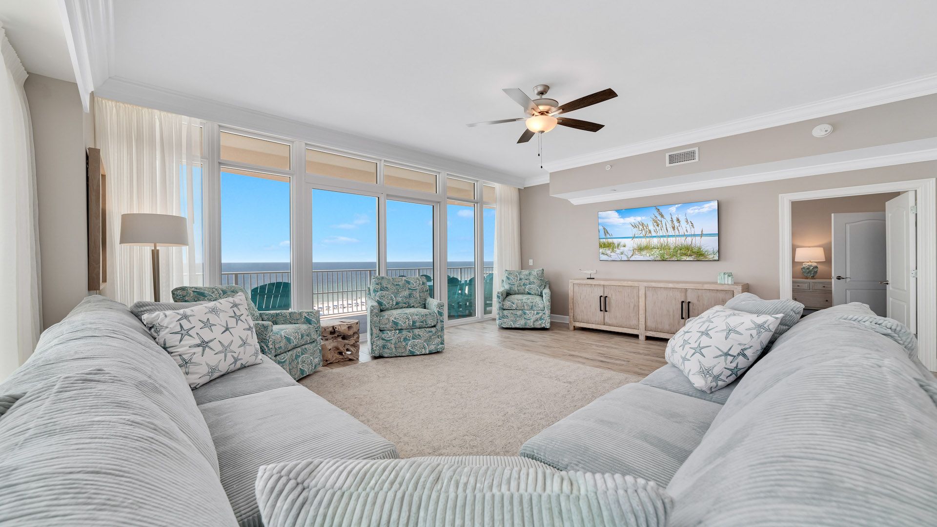 A spacious living room with a large window, a ceiling fan, and a view of the ocean.
