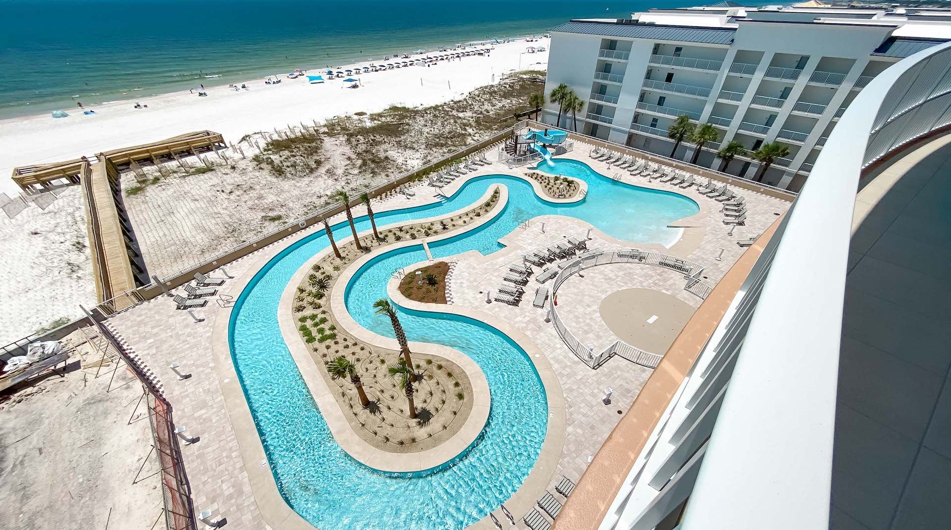 A resort with a large, winding pool, a beach, and a modern building with balconies.