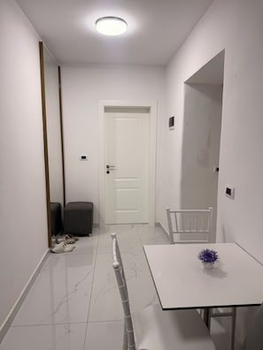 A modern, minimalist hallway with a white door, a small table with a vase, and a chair. - Comfortable Stay near Tirana City Center - Great Location (Tiranë)
