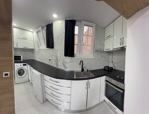 A compact kitchen with a curved countertop, built-in appliances, and a window with curtains. - Comfortable Stay near Tirana City Center - Great Location (Tiranë)