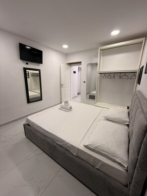 A modern bedroom with a bed, a TV mounted on the wall, a mirror, and a wardrobe with a hanging rack. - Comfortable Stay near Tirana City Center - Great Location (Tiranë)