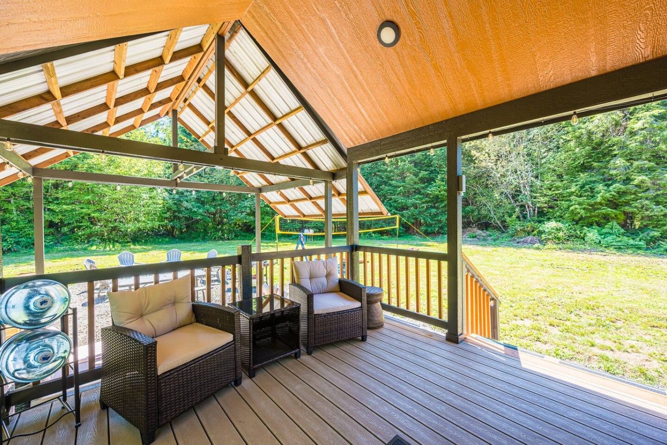 A covered outdoor deck with wicker furniture and a view of a grassy area.