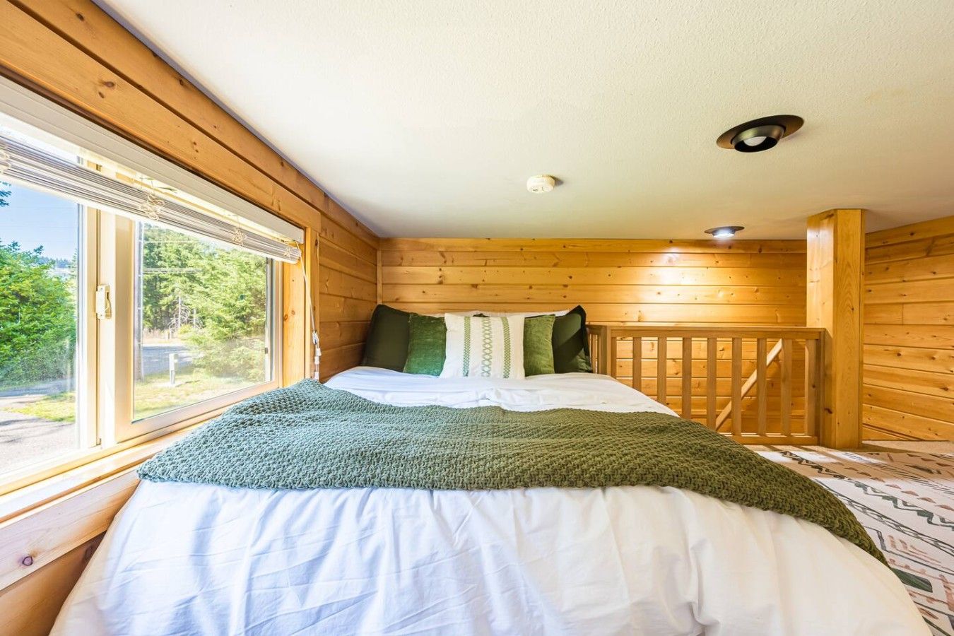 Un dormitorio de cabaña de madera con cama, ventana y barandilla de madera.
